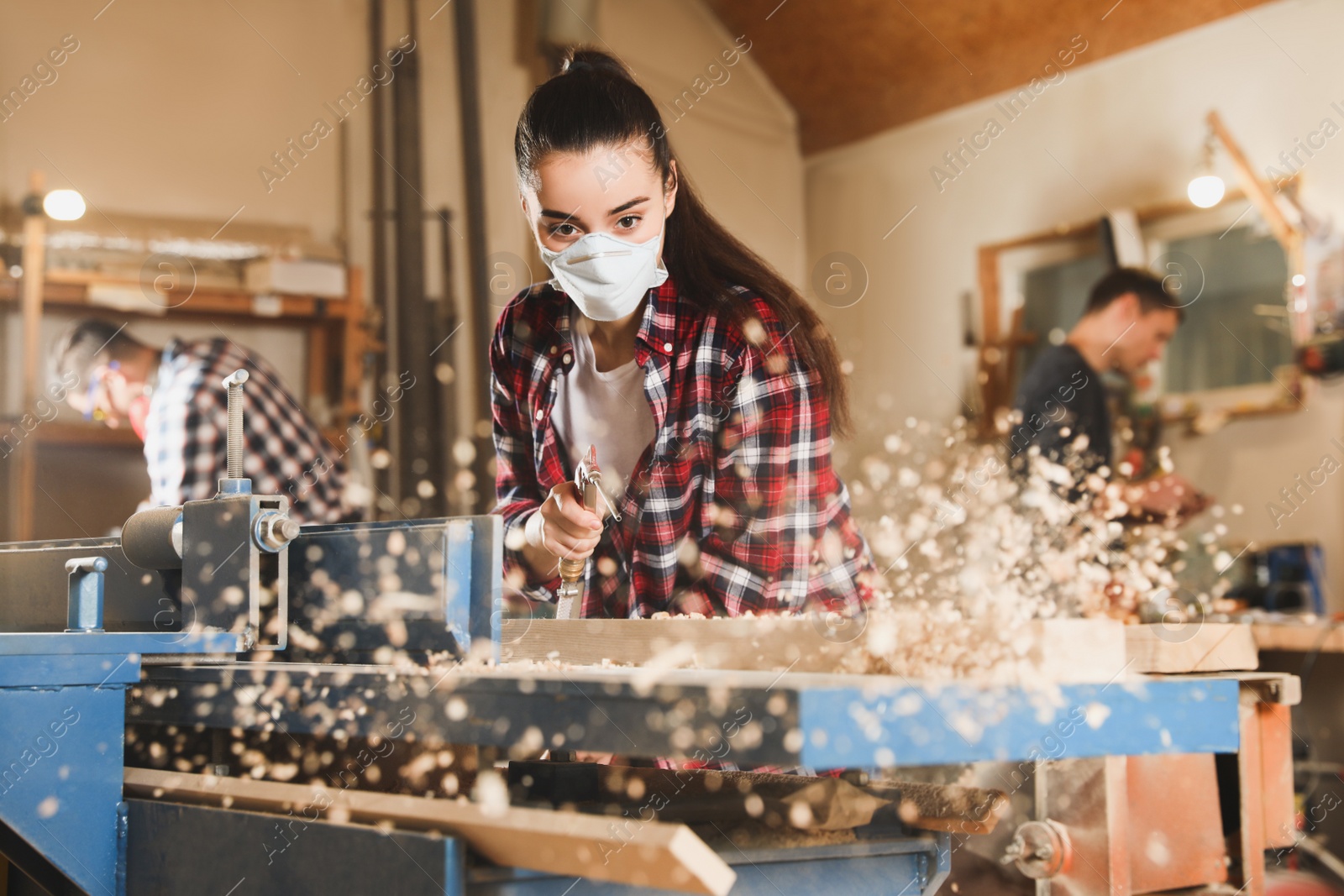 Photo of Female carpenter cleaning surface planer with air blow gun in workshop