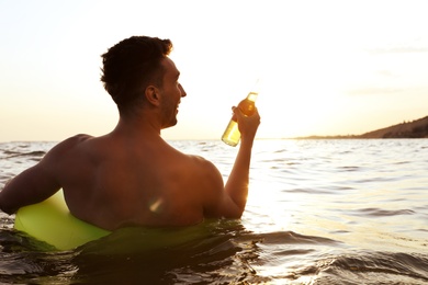 Photo of Young man with drink on inflatable ring in sea