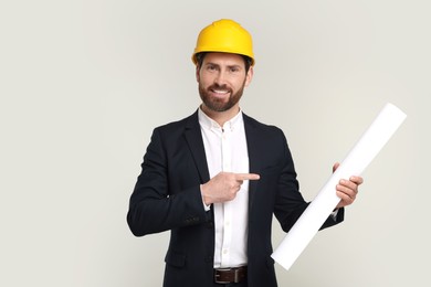 Photo of Architect in hard hat pointing at draft on gray background