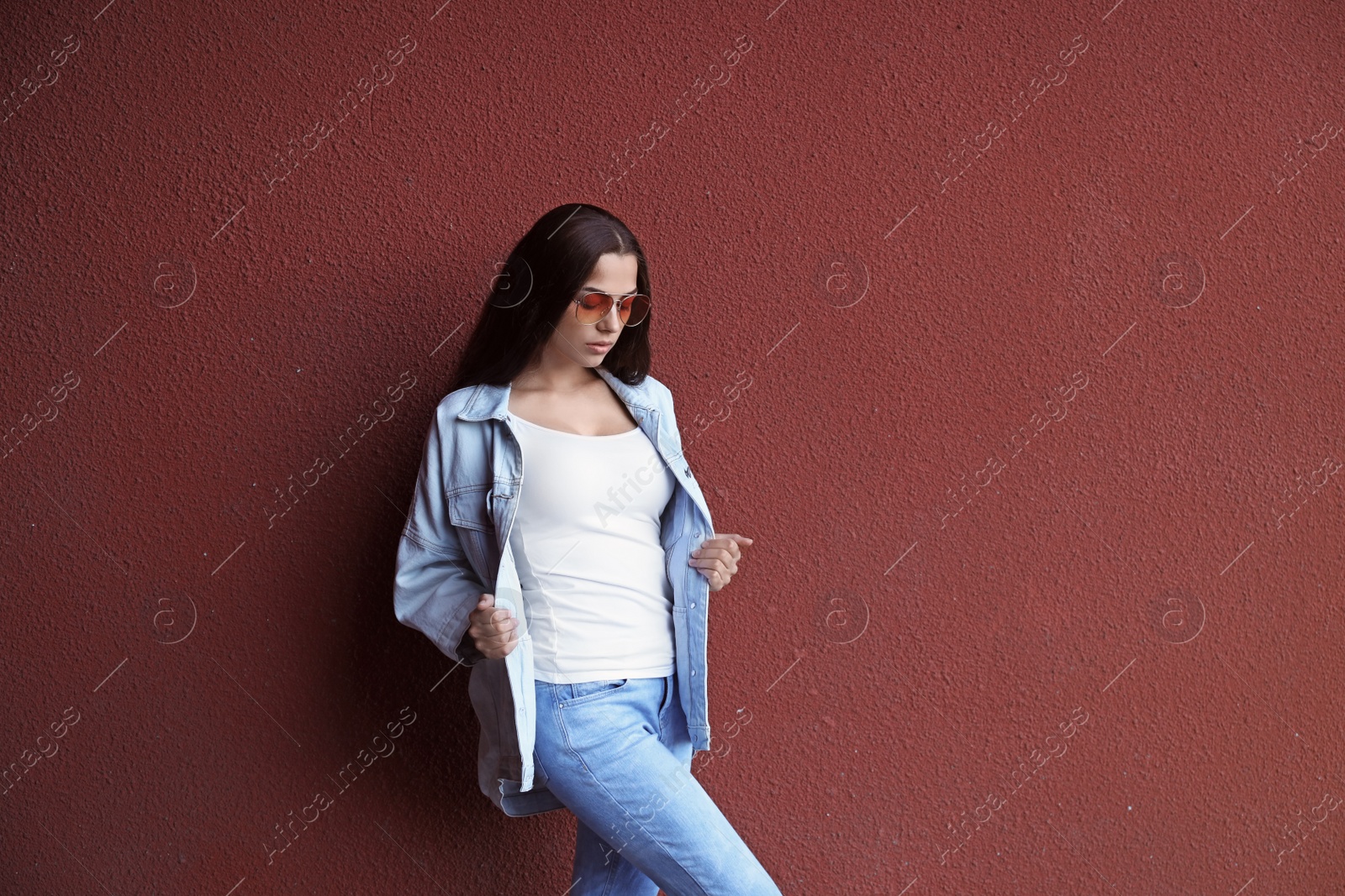 Photo of Young hipster woman in stylish jeans and jacket posing near color wall