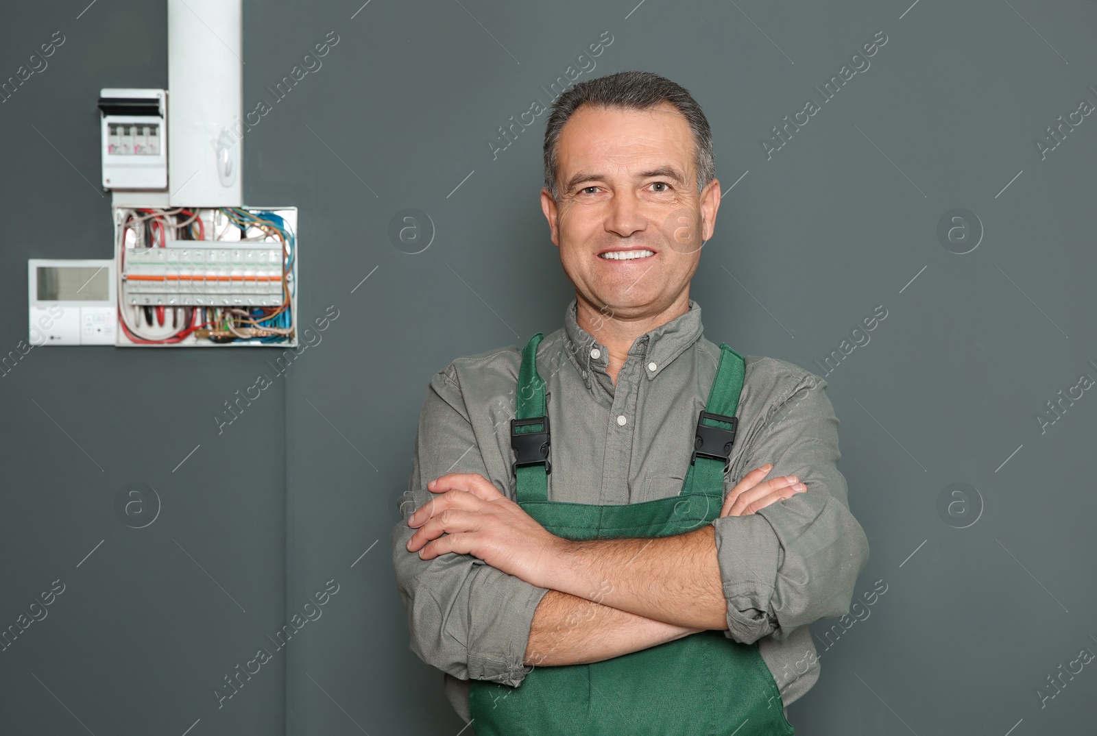 Photo of Male electrician standing near fuse board on grey wall