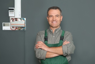 Male electrician standing near fuse board on grey wall