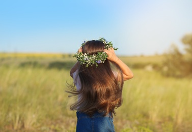 Photo of Cute little girl wearing flower wreath outdoors, back view. Child spending time in nature