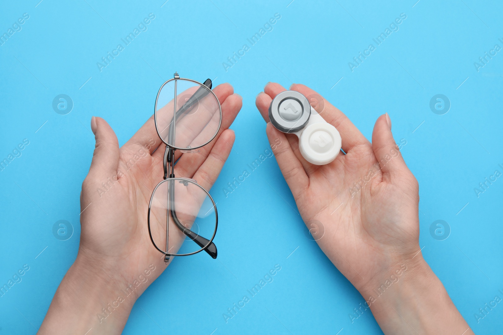 Photo of Woman holding case with contact lenses and glasses on light blue background, top view