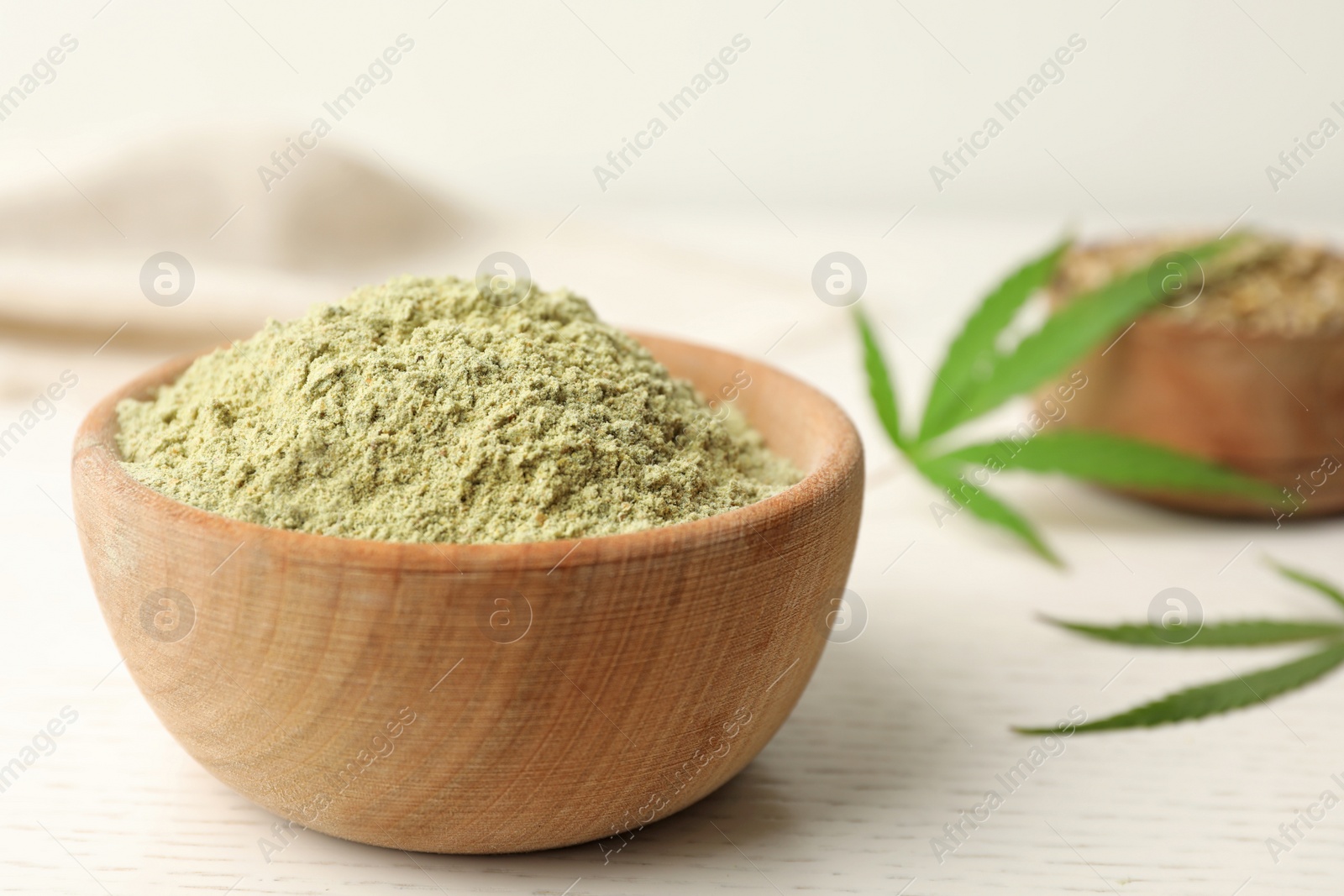 Photo of Bowl of hemp protein powder on white wooden table, closeup