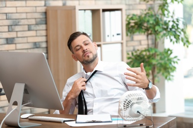 Businessman suffering from heat in front of small fan at workplace