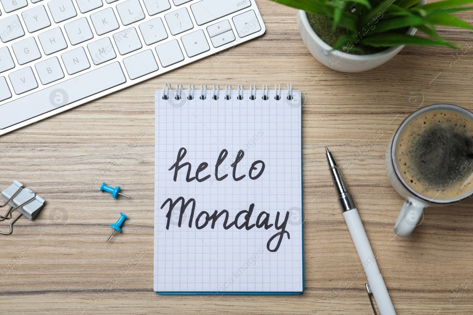 Photo of Message Hello Monday written in notebook, computer keyboard and cup of coffee on wooden desk, flat lay