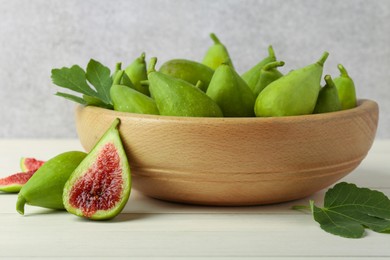 Cut and whole fresh green figs on white wooden table near grey wall