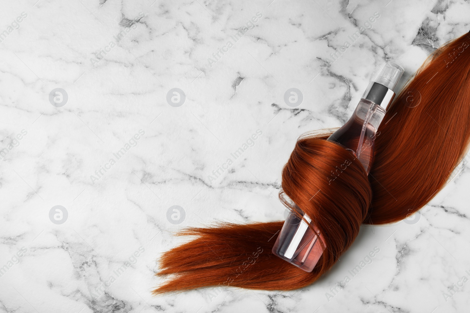 Photo of Spray bottle wrapped in lock of hair on white marble background, flat lay with space for text. Natural cosmetic products