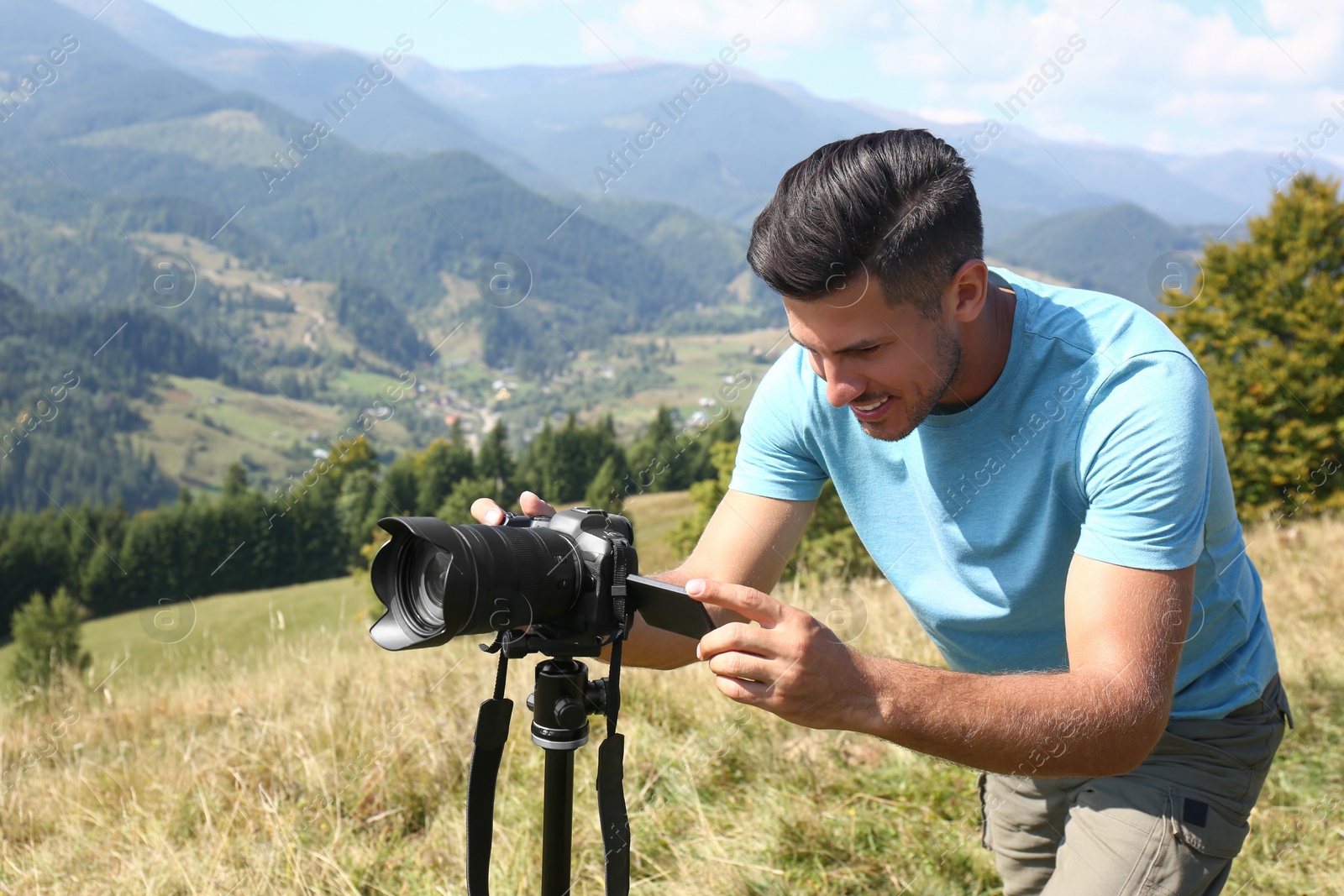 Photo of Man taking photo of mountain landscape with modern camera on tripod outdoors