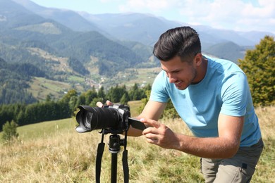 Man taking photo of mountain landscape with modern camera on tripod outdoors