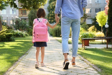 Father taking his little child to school through park