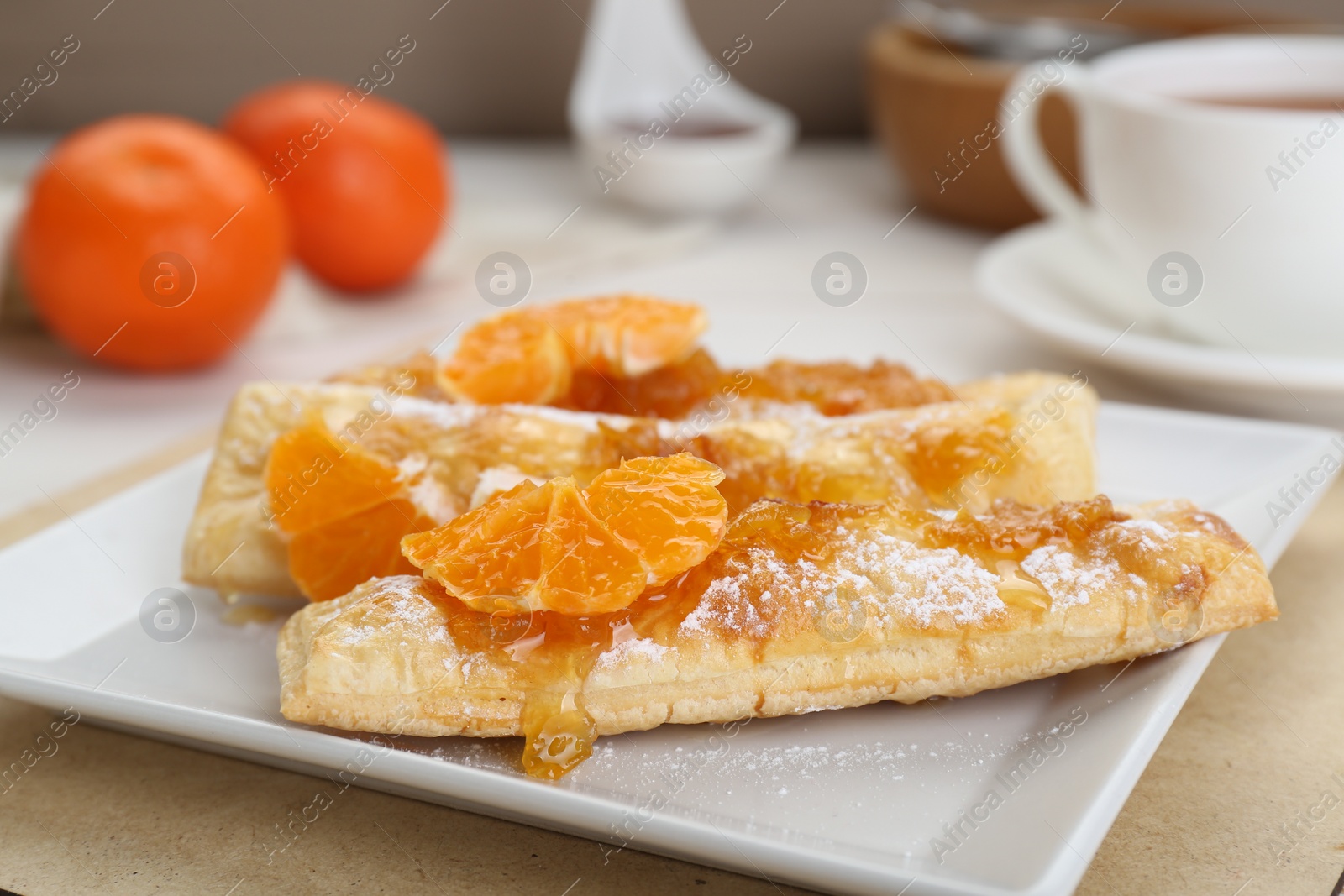 Photo of Fresh tasty puff pastry with sugar powder and tangerines on table, closeup