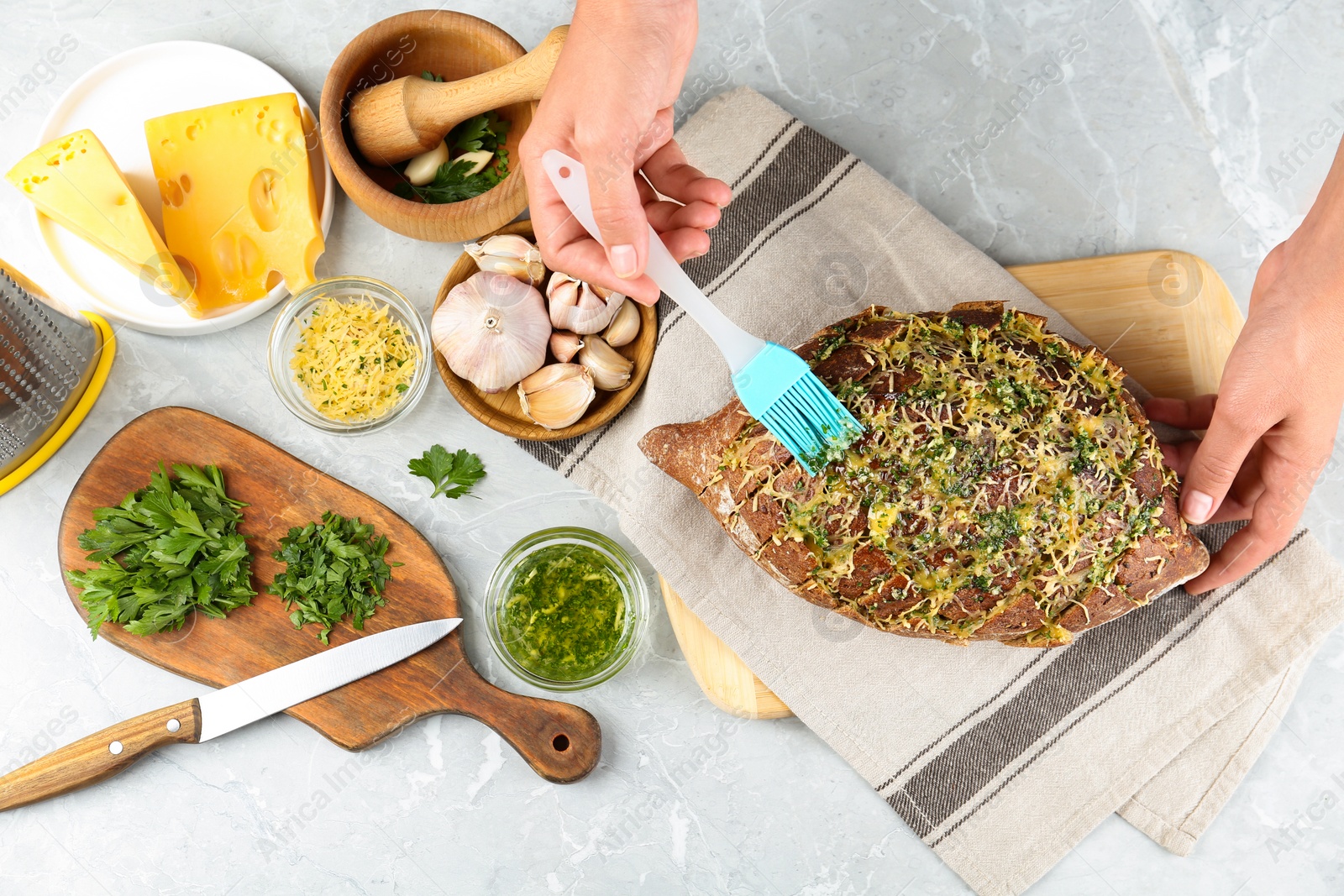 Photo of Woman brushing tasty homemade bread with garlic and herbs at light table, top view