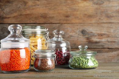 Glass jars with different types of groats and pasta on wooden table
