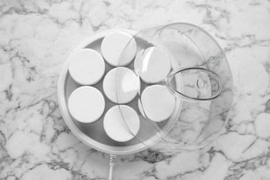 Modern yogurt maker with jars on white marble table, top view