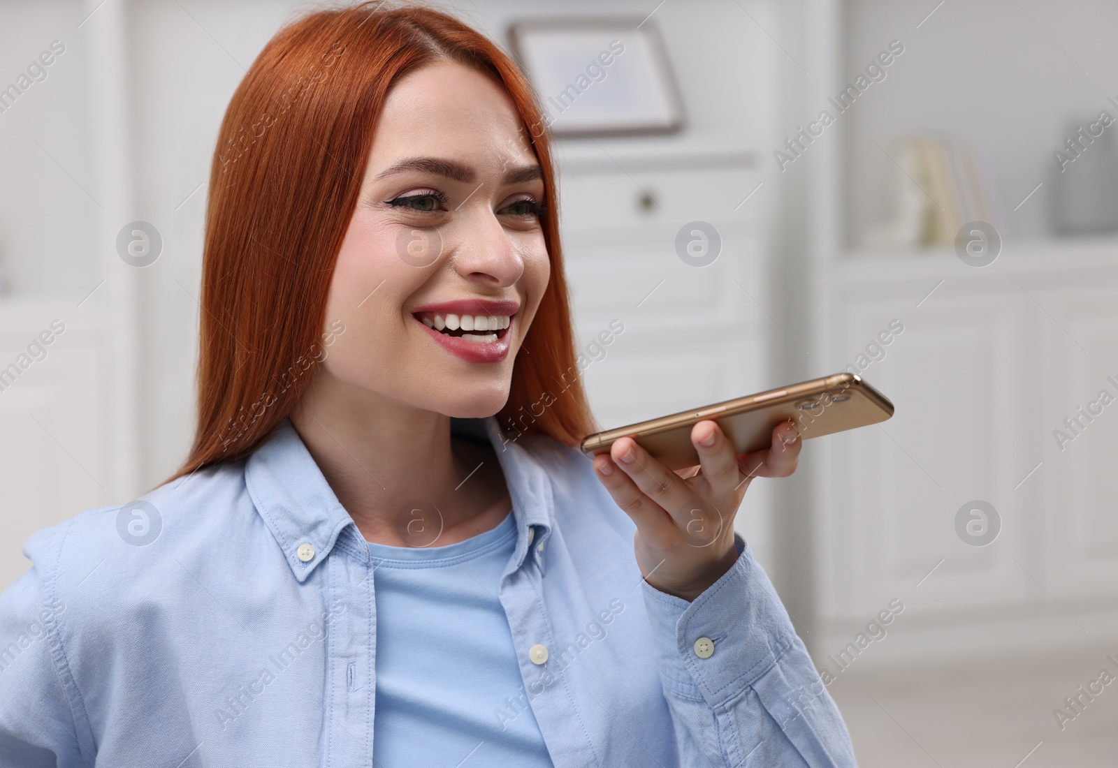 Photo of Happy woman sending voice message via smartphone at home