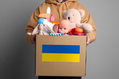 Image of Humanitarian aid for Ukrainian refugees. Man holding donation box full of different toys on grey background, closeup