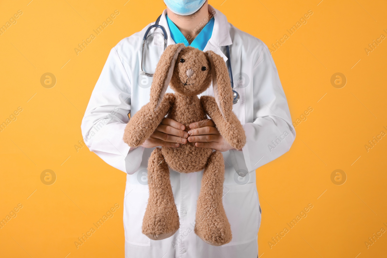 Photo of Pediatrician with toy bunny and stethoscope on yellow background, closeup