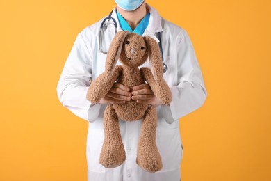 Photo of Pediatrician with toy bunny and stethoscope on yellow background, closeup