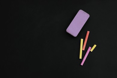 Colorful chalks and duster on black board, flat lay. Space for text