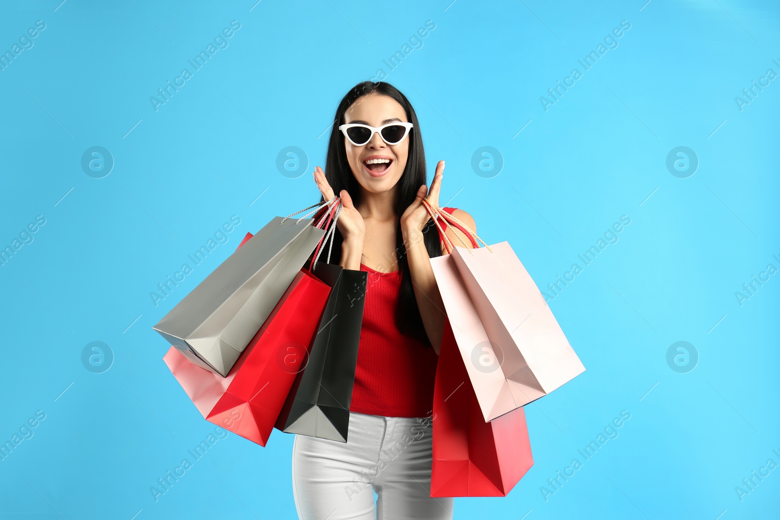 Photo of Excited young woman with paper shopping bags on light blue background