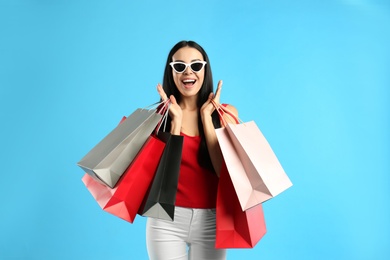 Photo of Excited young woman with paper shopping bags on light blue background