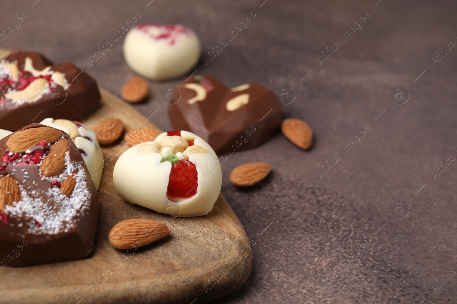 Photo of Tasty chocolate heart shaped candies with nuts on brown textured table, closeup. Space for text