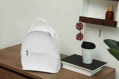 Photo of Stylish urban backpack on wooden chest of drawers in hallway