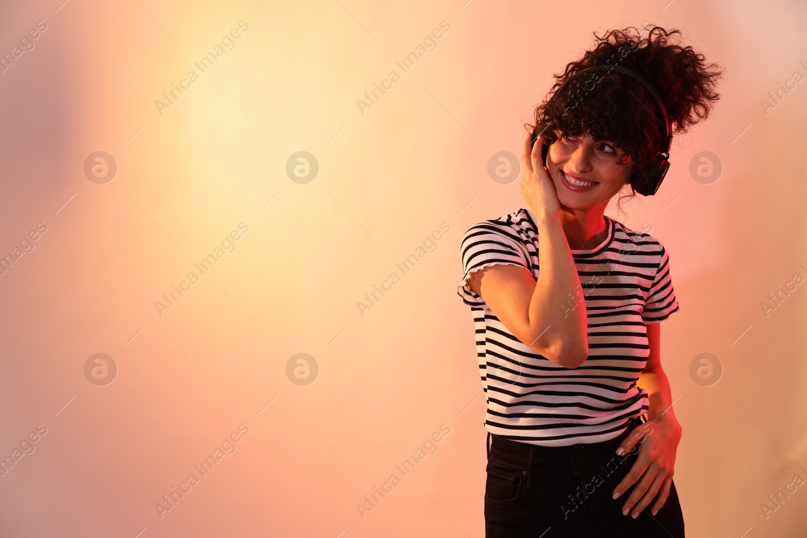 Photo of Beautiful young woman listening to music with headphones on color background in neon lights. Space for text