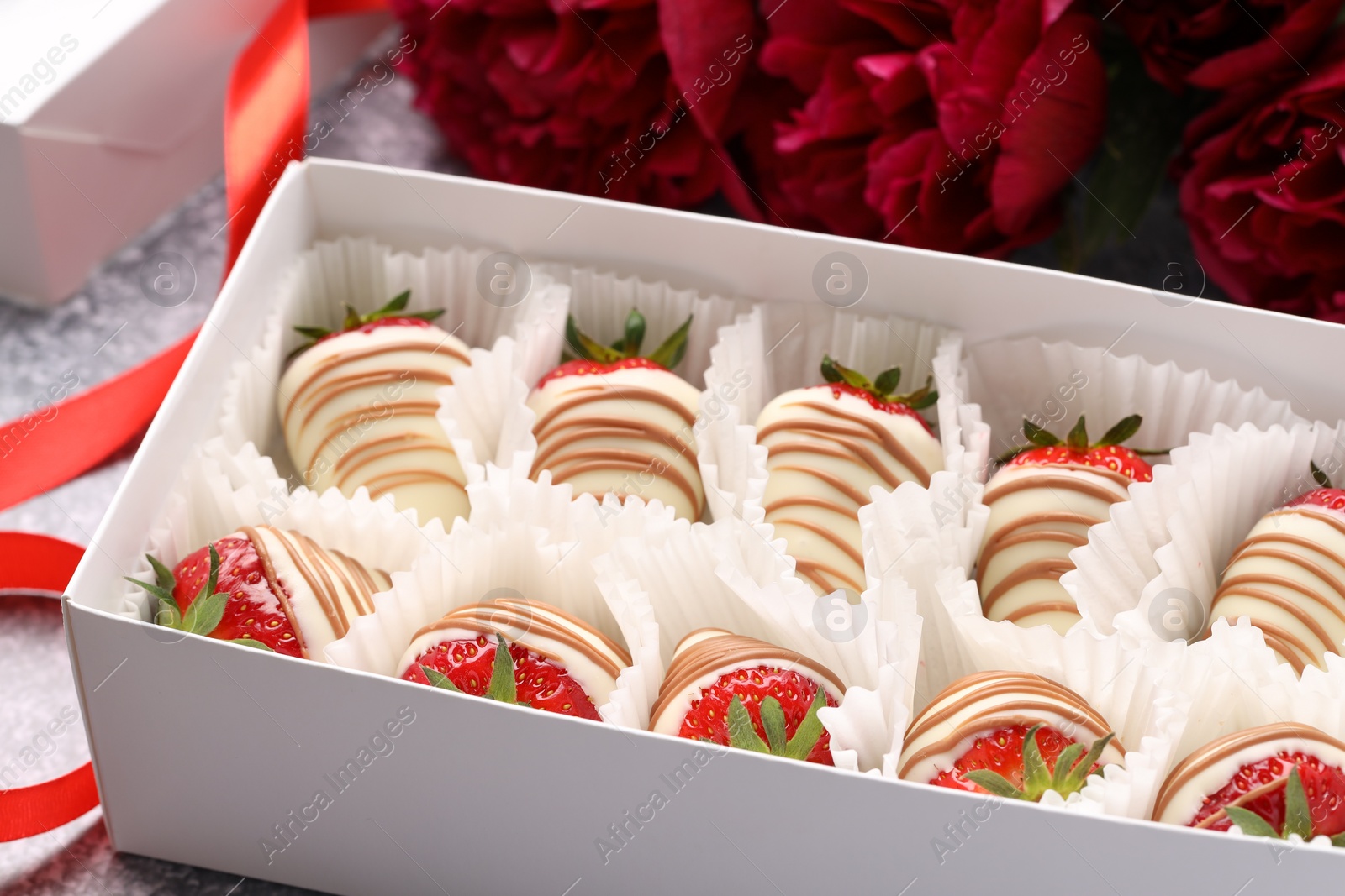 Photo of Delicious chocolate covered strawberries in box and flowers on table, closeup