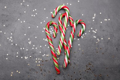 Many sweet Christmas candy canes and shiny confetti on grey background, flat lay