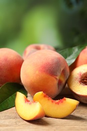 Cut and whole fresh ripe peaches with green leaves on wooden table against blurred background, closeup. Space for text