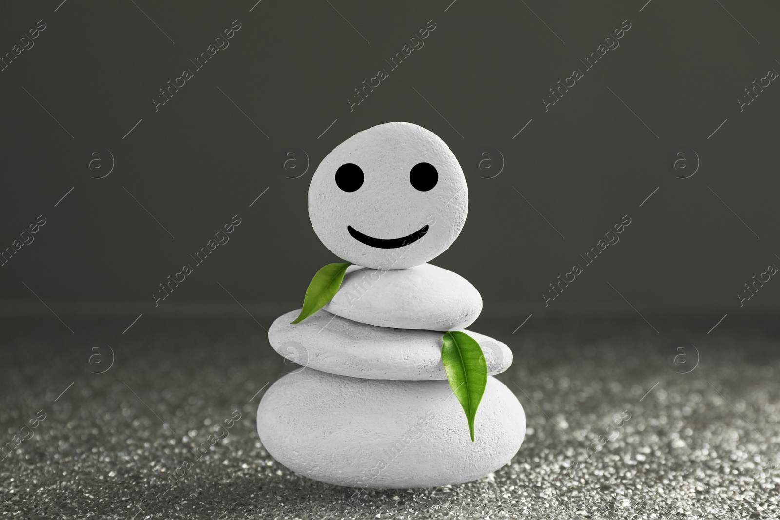 Photo of Stack of stones with drawn happy face and green leaves on grey background. Zen concept