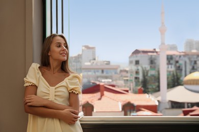 Photo of Beautiful young woman standing on balcony, space for text