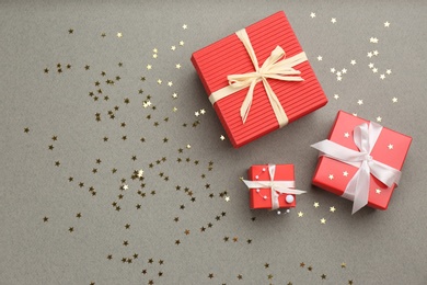Photo of Christmas gift boxes and shiny confetti on grey background, flat lay. Space for text