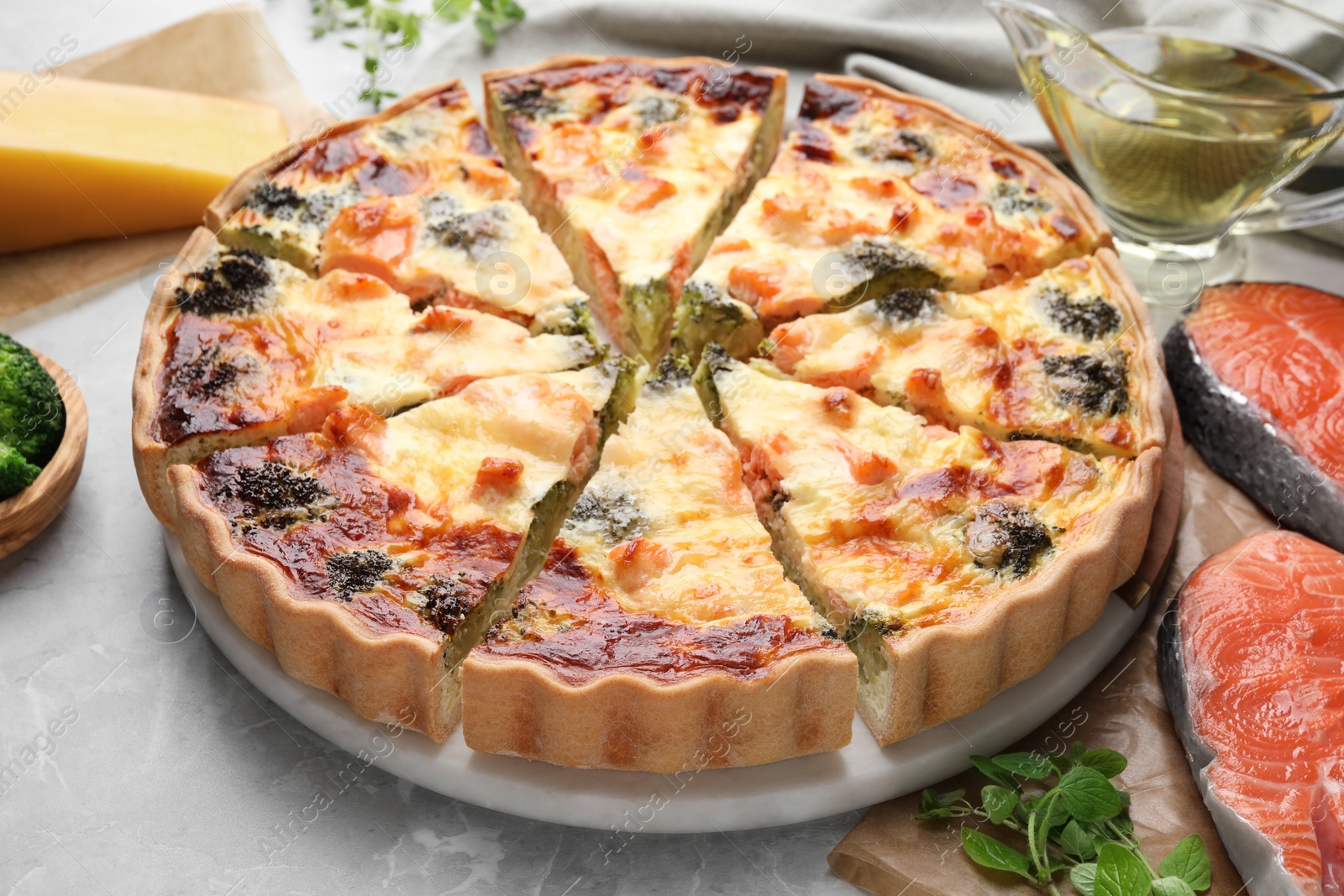 Photo of Delicious homemade quiche and ingredients on light gray table