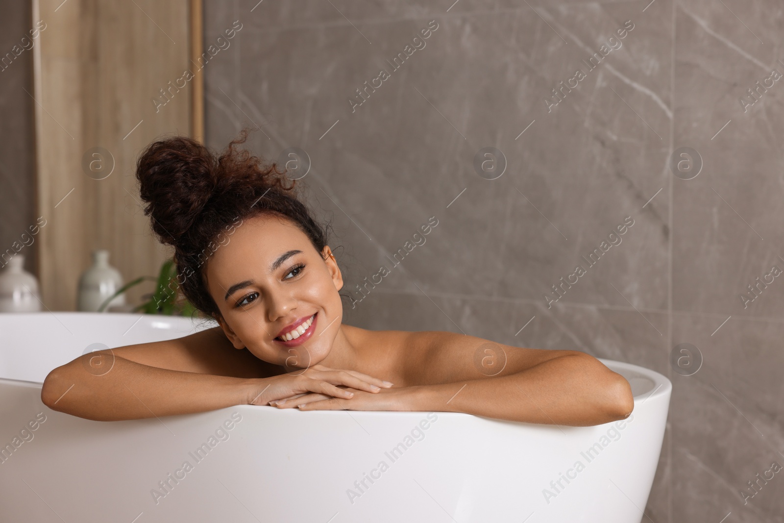 Photo of Beautiful African American woman taking bath indoors, space for text