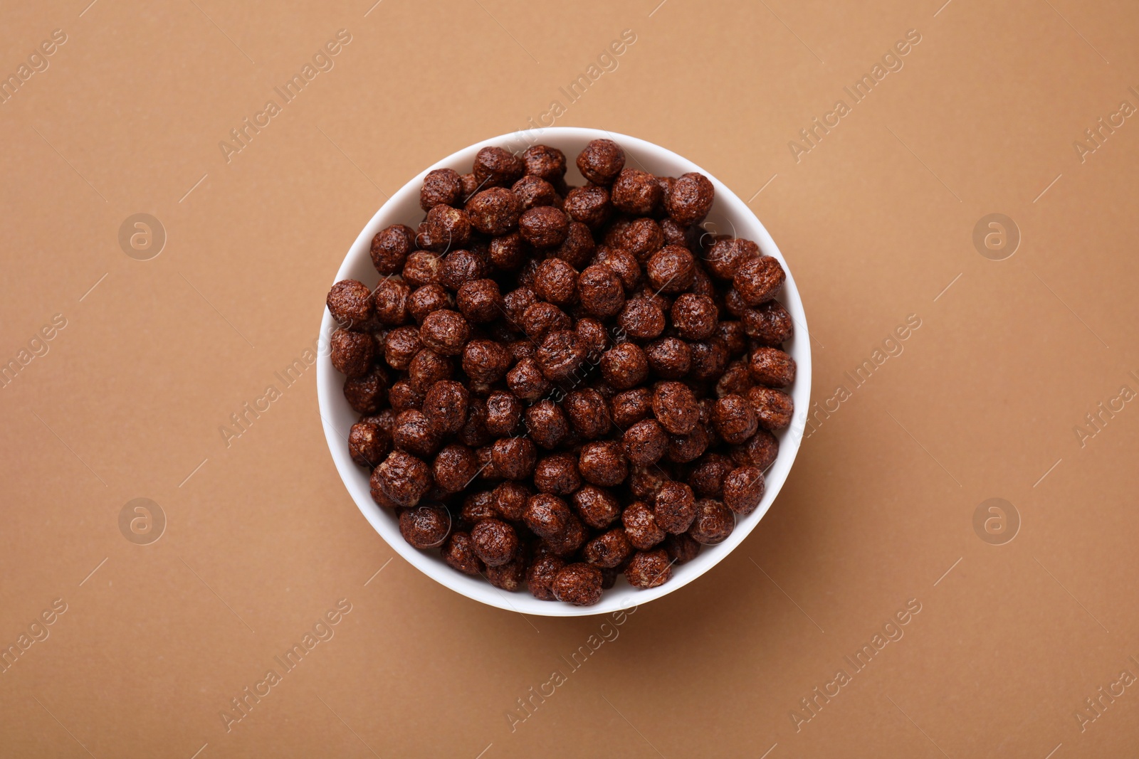 Photo of Chocolate cereal balls in bowl on brown table, top view