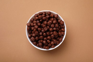 Photo of Chocolate cereal balls in bowl on brown table, top view