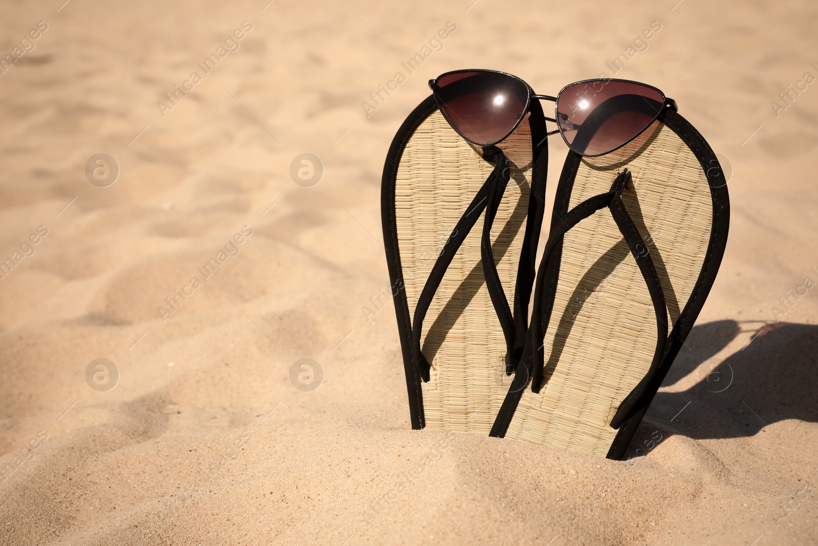 Photo of Flip flops and sunglasses on sandy sea shore, space for text. Beach accessories