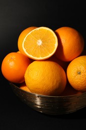 Photo of Bowl with ripe juicy oranges on black background