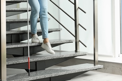 Photo of Blind person with long cane going down stairs indoors, closeup