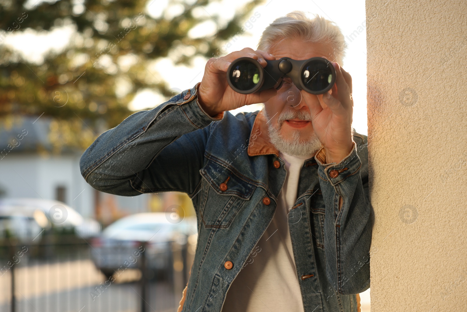 Photo of Concept of private life. Curious senior man with binoculars spying on neighbours outdoors