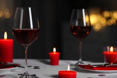 Romantic table setting with glasses of red wine and burning candles against blurred lights