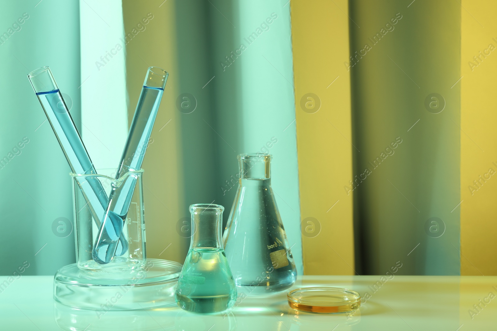 Photo of Laboratory analysis. Different glassware on table against color background, space for text