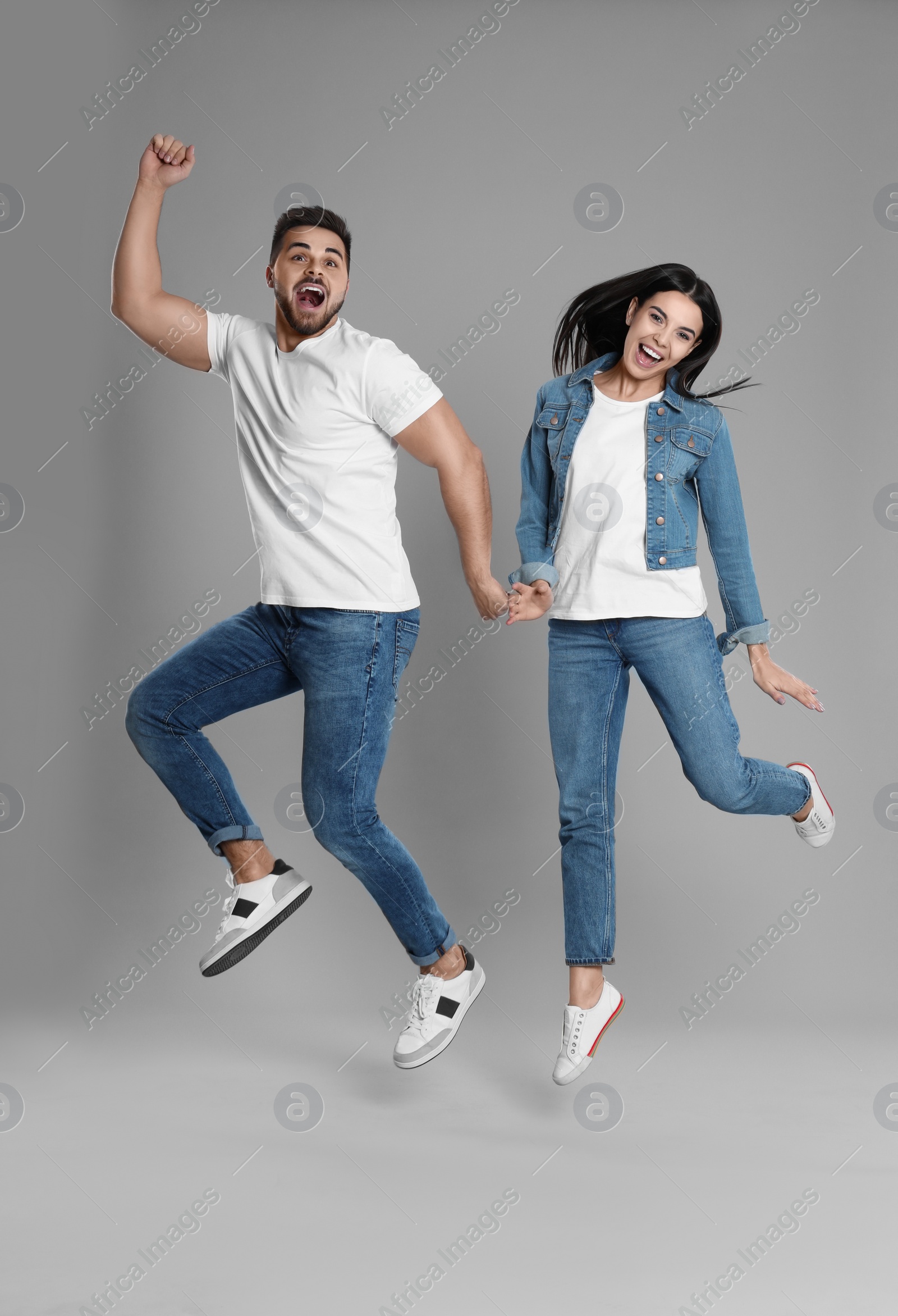 Photo of Young couple in stylish jeans jumping on grey background