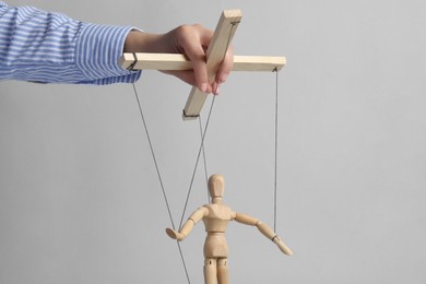 Woman pulling strings of puppet on light grey background, closeup