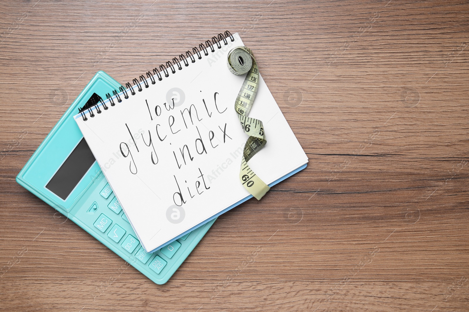 Photo of Notebook with words Low Glycemic Index Diet, measuring tape and calculator on wooden table, flat lay. Space for text