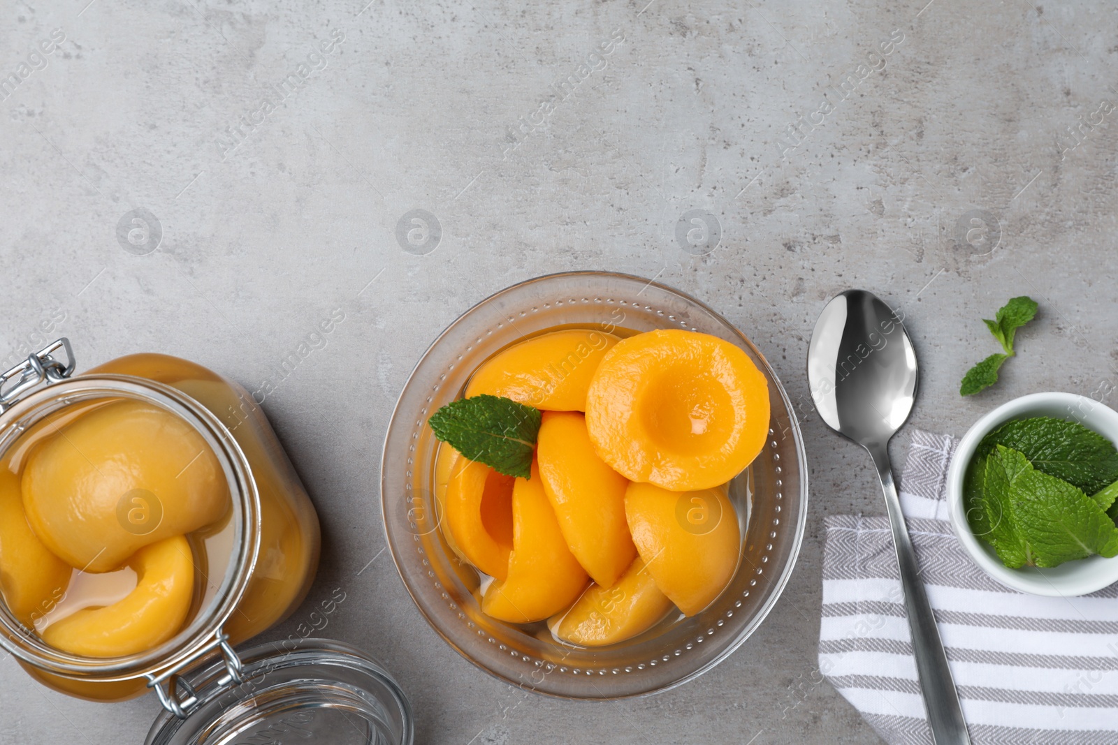 Photo of Canned peach halves in bowl and jar on grey table, flat lay. Space for text